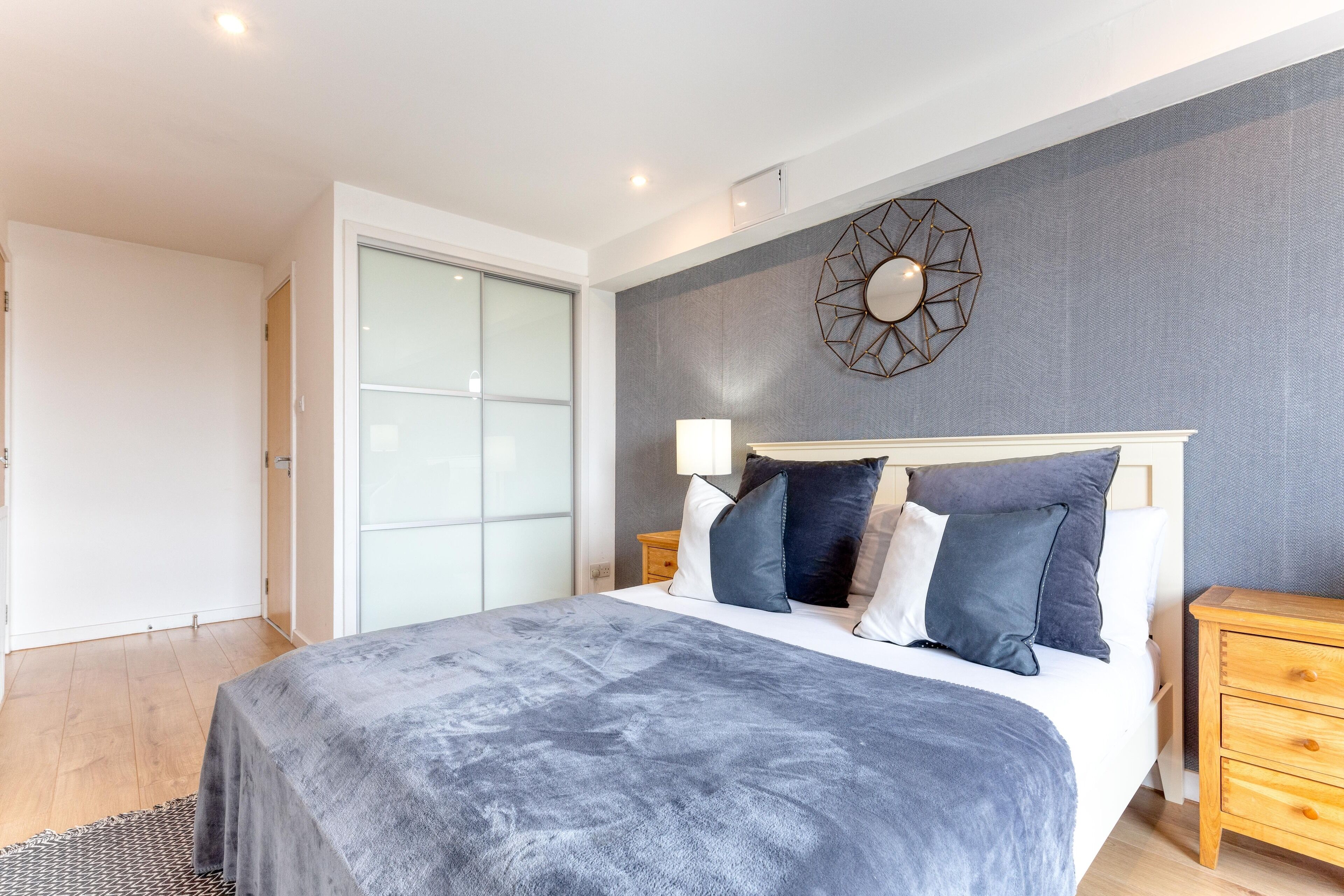 A modern bedroom with a large bed, a geometric wall decoration, and a wooden nightstand.