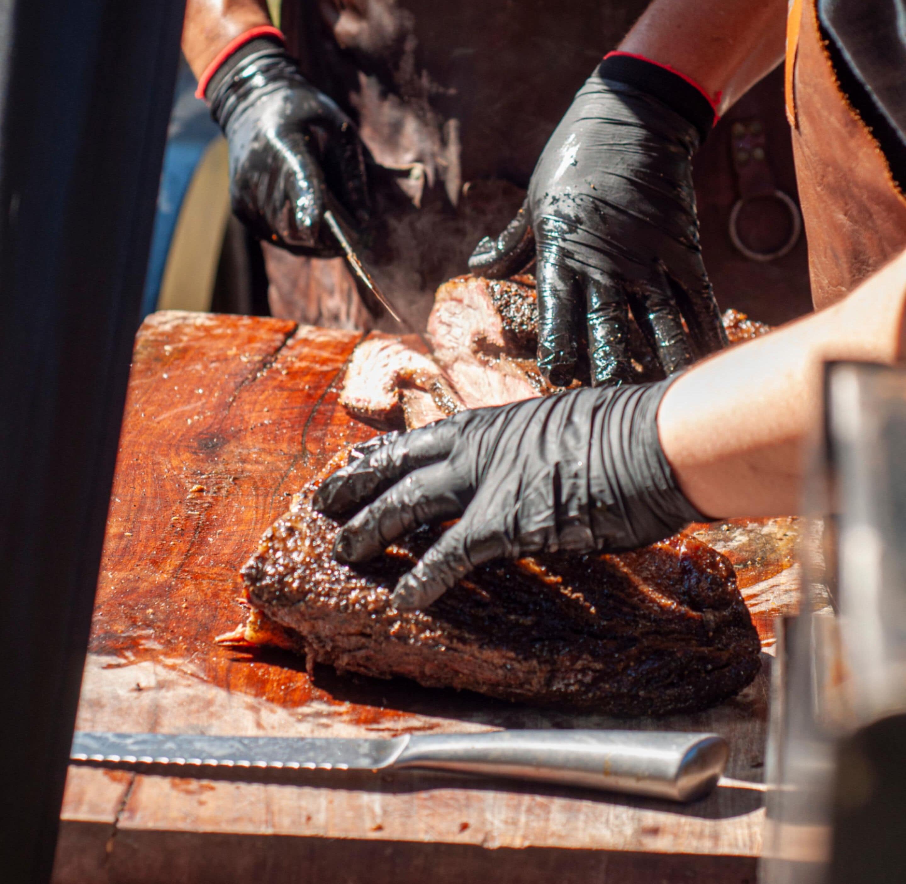 A person wearing black gloves handling a large piece of meat on a wooden cutting board.