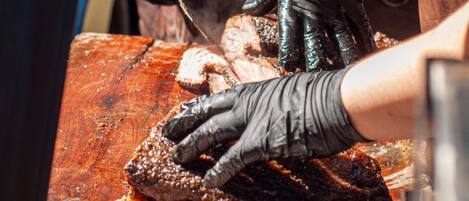 Una persona con guantes negros manipula un trozo grande de carne sobre una tabla de madera.