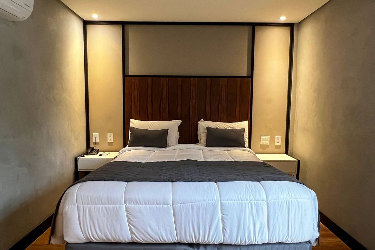 A modern hotel room with a large bed, two bedside tables, and a wooden headboard.