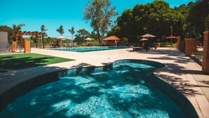 A swimming pool area with a curved pool, lounge chairs, and shaded seating areas.