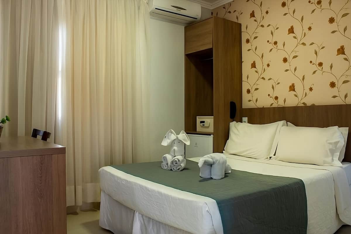 A hotel room with a bed, a desk, and a wall-mounted air conditioner.