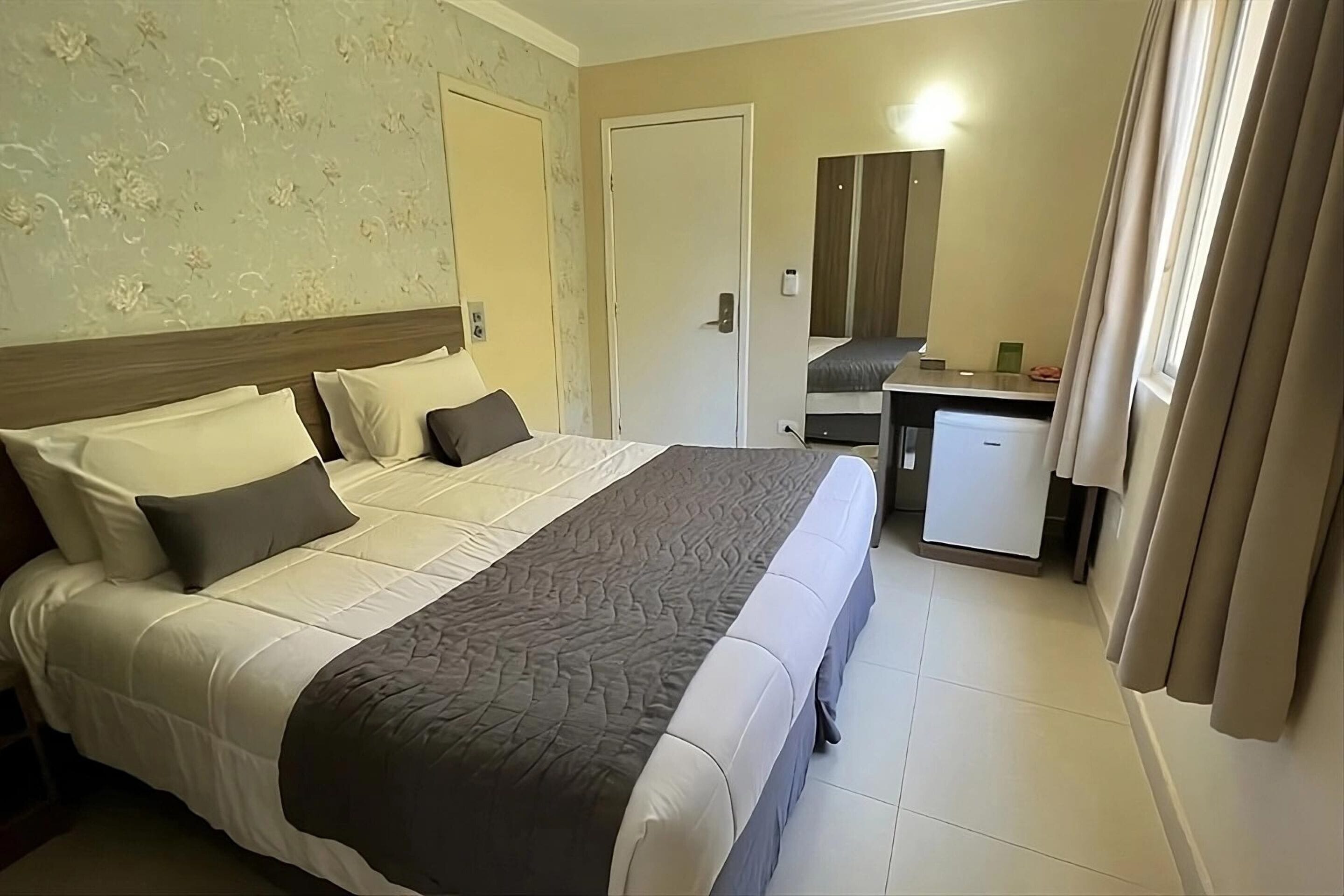 A hotel room with a large bed, a desk, and a mirror.