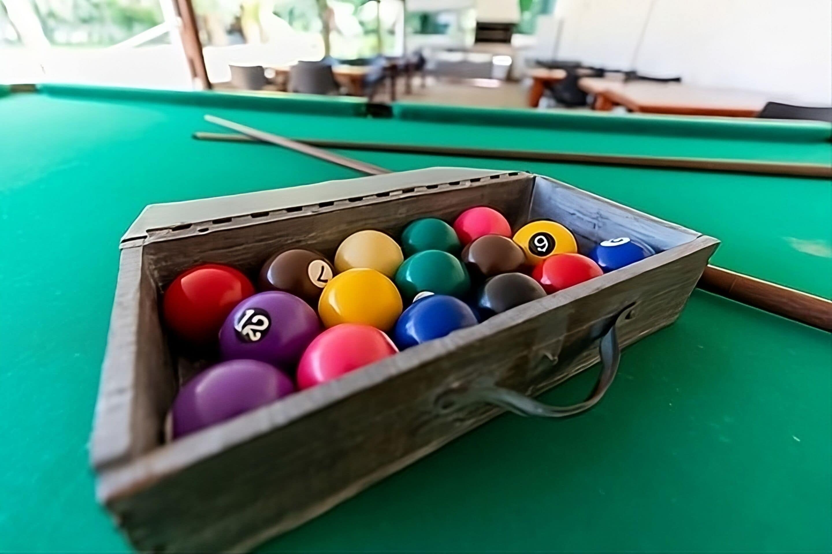 A wooden pool table with a cue stick and a rack of colorful billiard balls.