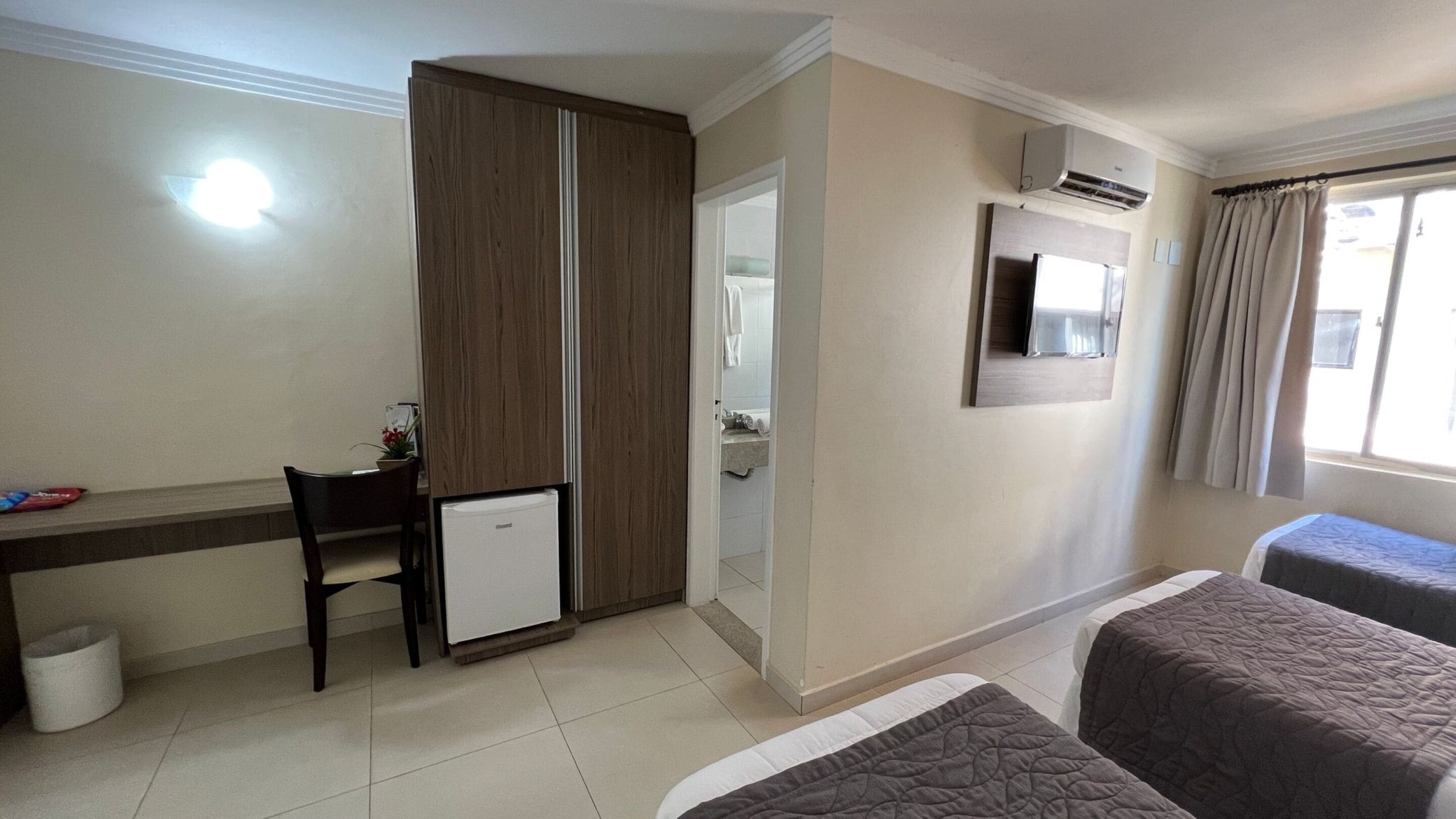 Habitación de hotel con escritorio, refrigerador pequeño, cama con colcha, espejo y aire acondicionado.