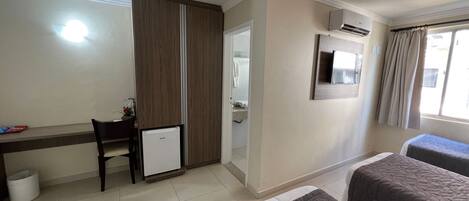 Habitación de hotel con escritorio, refrigerador pequeño, cama con colcha, espejo y aire acondicionado.