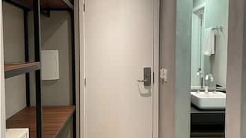 A narrow hallway with a white door, wooden shelves, a microwave, and a sink visible through a glass partition.