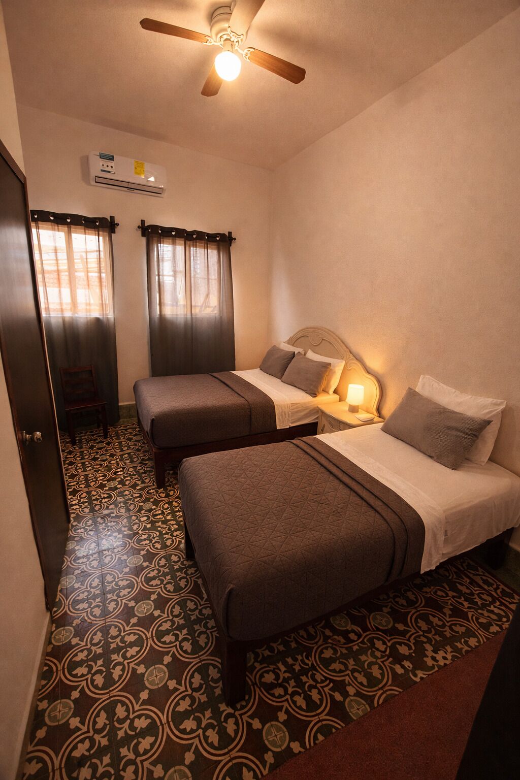 A hotel room with two beds, a ceiling fan, an air conditioning unit, and patterned flooring.