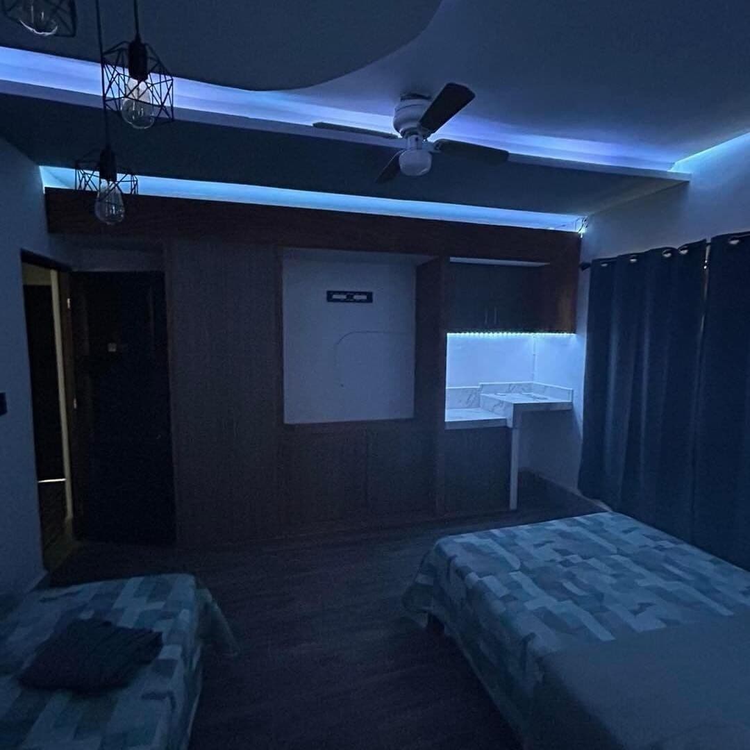A hotel room with two beds, a ceiling fan, a wall-mounted TV, and a bathroom with a shower curtain.