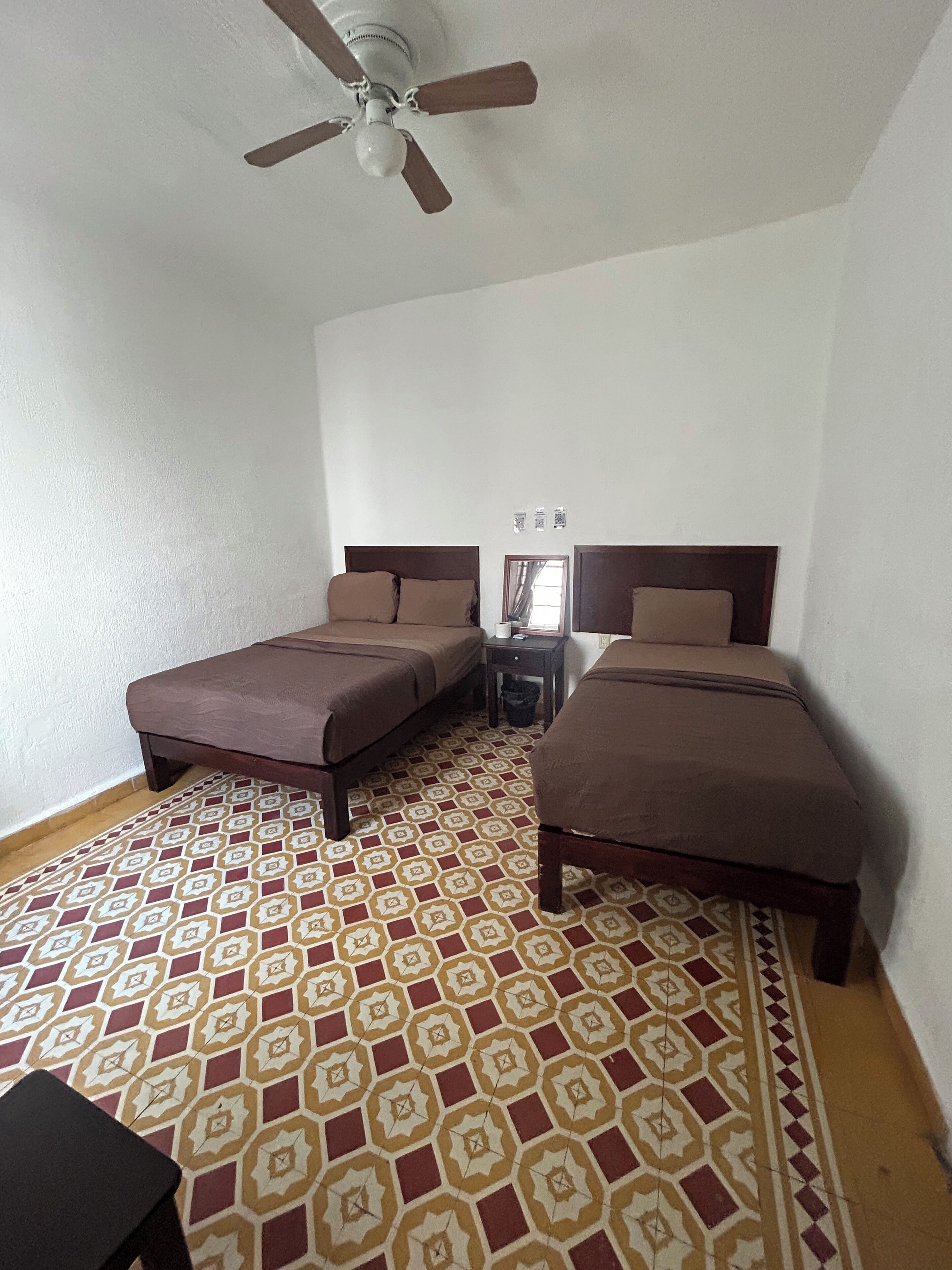 Un dormitorio con dos camas, ventilador de techo y suelo estampado.