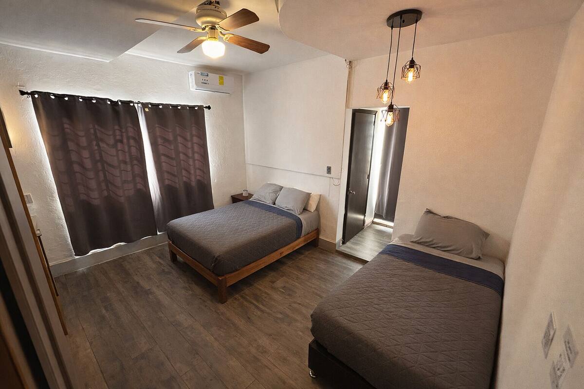 A compact bedroom with a single bed, a smaller bed, a ceiling fan, and a wall-mounted light fixture.