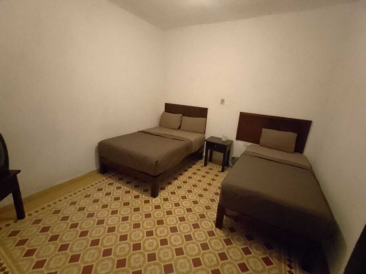Una habitación pequeña y tenuemente iluminada con dos camas individuales, una mesita y un suelo con diseño.