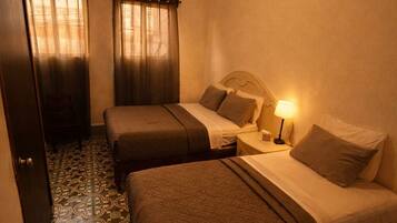 A hotel room with two beds, a ceiling fan, a nightstand with a lamp, and patterned floor tiles.
