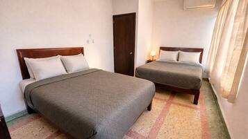 Habitación de hotel con dos camas, una puerta, un equipo de aire acondicionado y una ventana con cortinas.