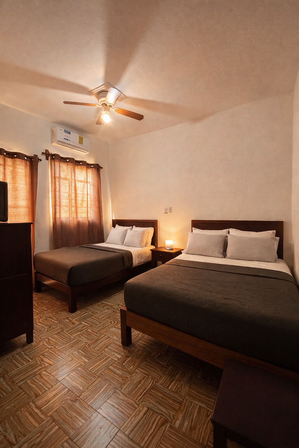Habitación de hotel con dos camas, ventilador de techo, unidad de aire acondicionado y suelo de parqué de madera.