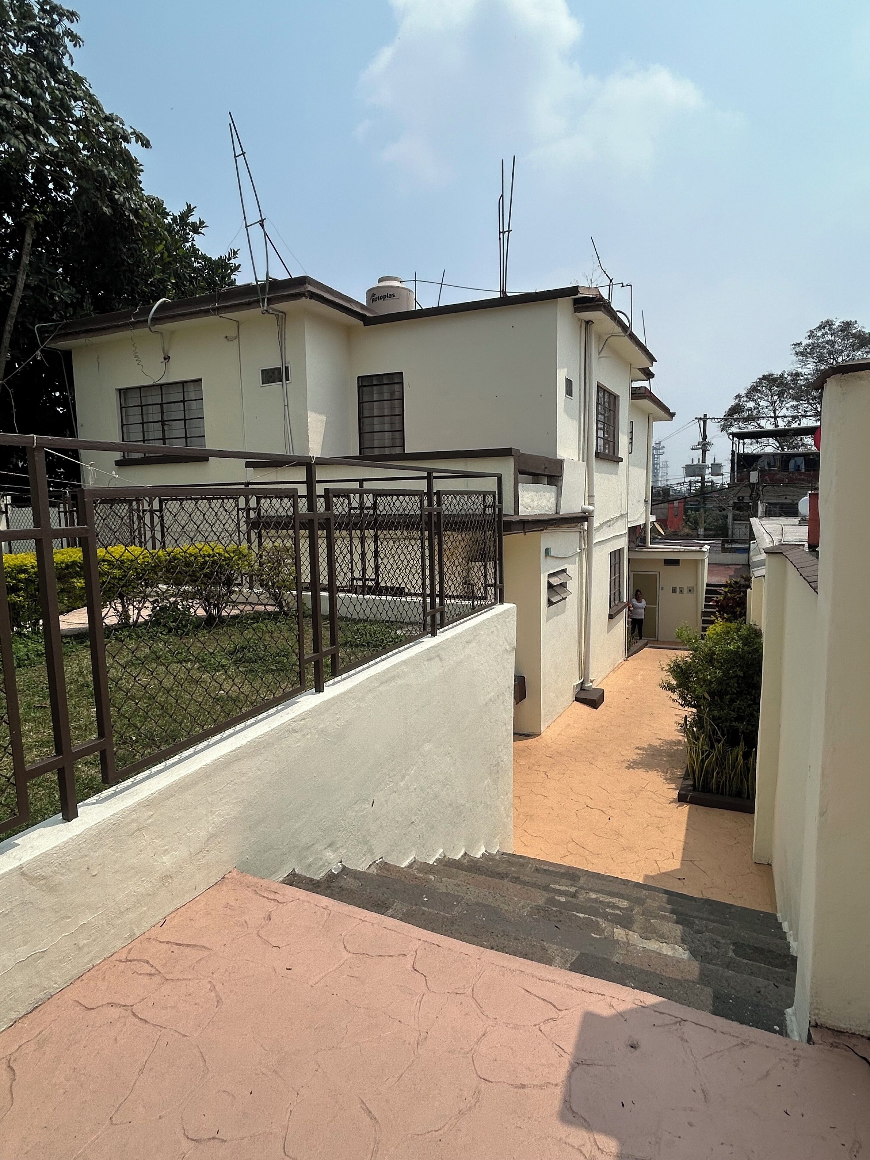 Un edificio de dos plantas con entrada porticada, un camino pavimentado y un pequeño jardín.