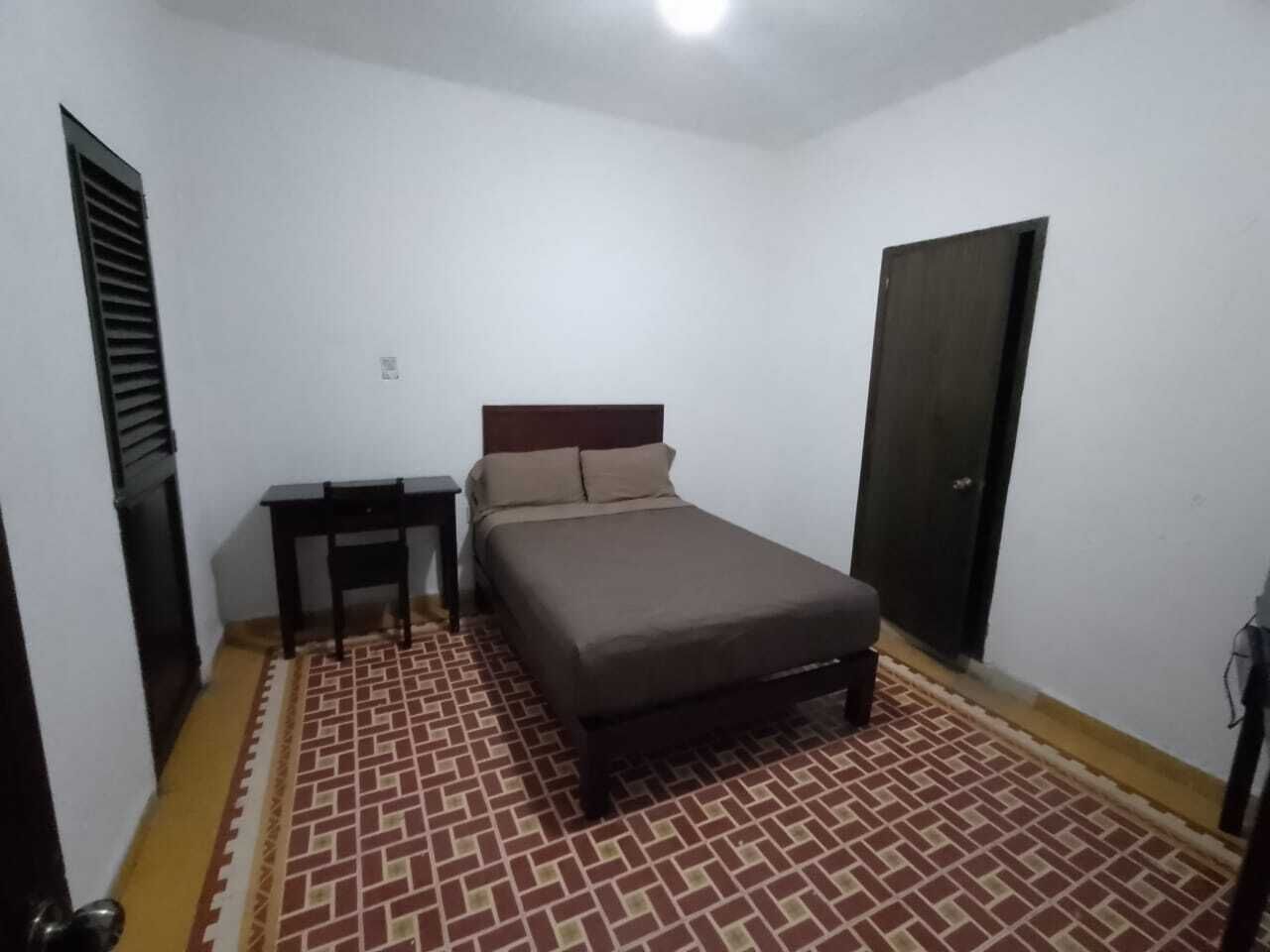 A bedroom with a bed, a nightstand, a door, and a patterned floor.