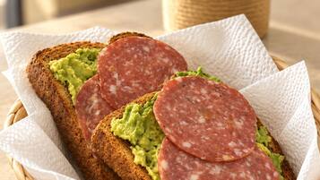 Un sándwich con salami en rodajas y guacamole sobre una rebanada de pan, dentro de una cesta tejida.
