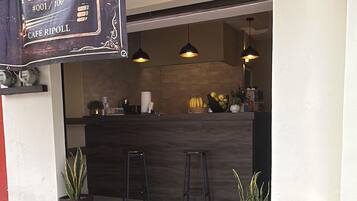 A café with a dark counter, hanging pendant lights, and potted plants.