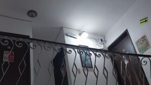 Una escala amb barana metàl·lica decorativa, una làmpada al sostre i una porta amb un rètol a la part superior.