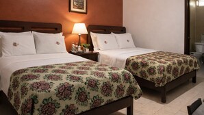 Habitació d'hotel amb dos llits, un ventilador de sostre, una tauleta de nit amb una làmpada i un quadre a la paret.