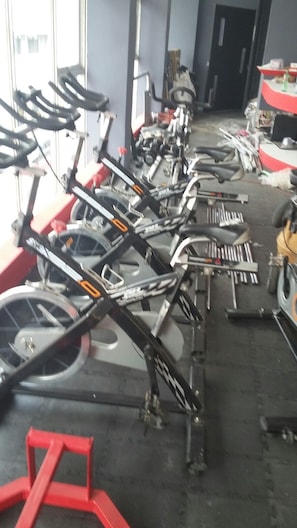 A row of stationary bikes in a gym with a black floor and a red structure in the foreground.