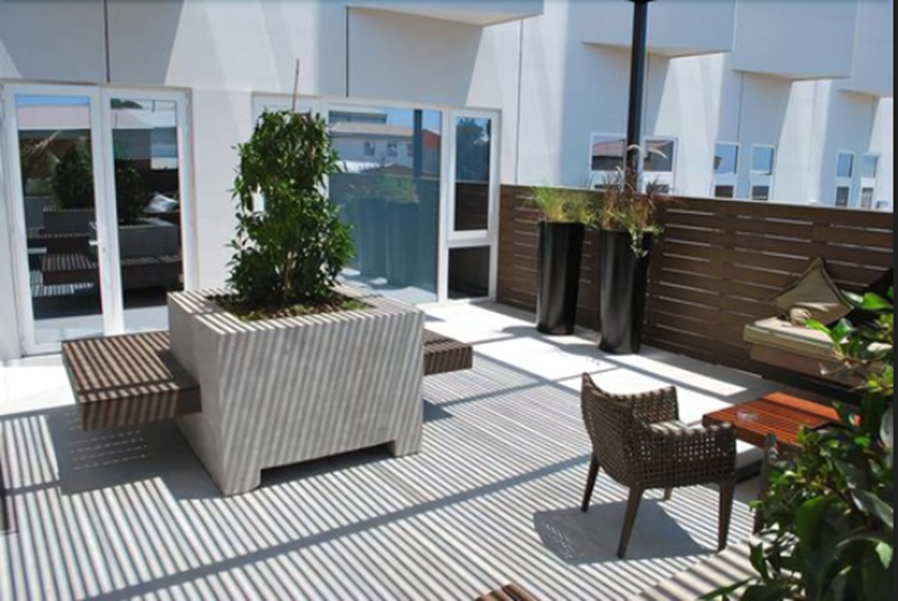 A modern outdoor patio with a large planter, wicker furniture, and a view of the cityscape.