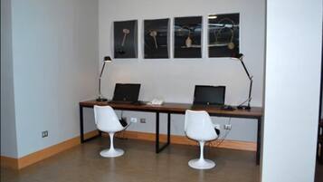 Et moderne kontorrum med to skriveborde, hvert med en computer og en lampe, samt to hvide stole.