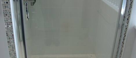 A glass-enclosed shower with a tiled floor and a drain.