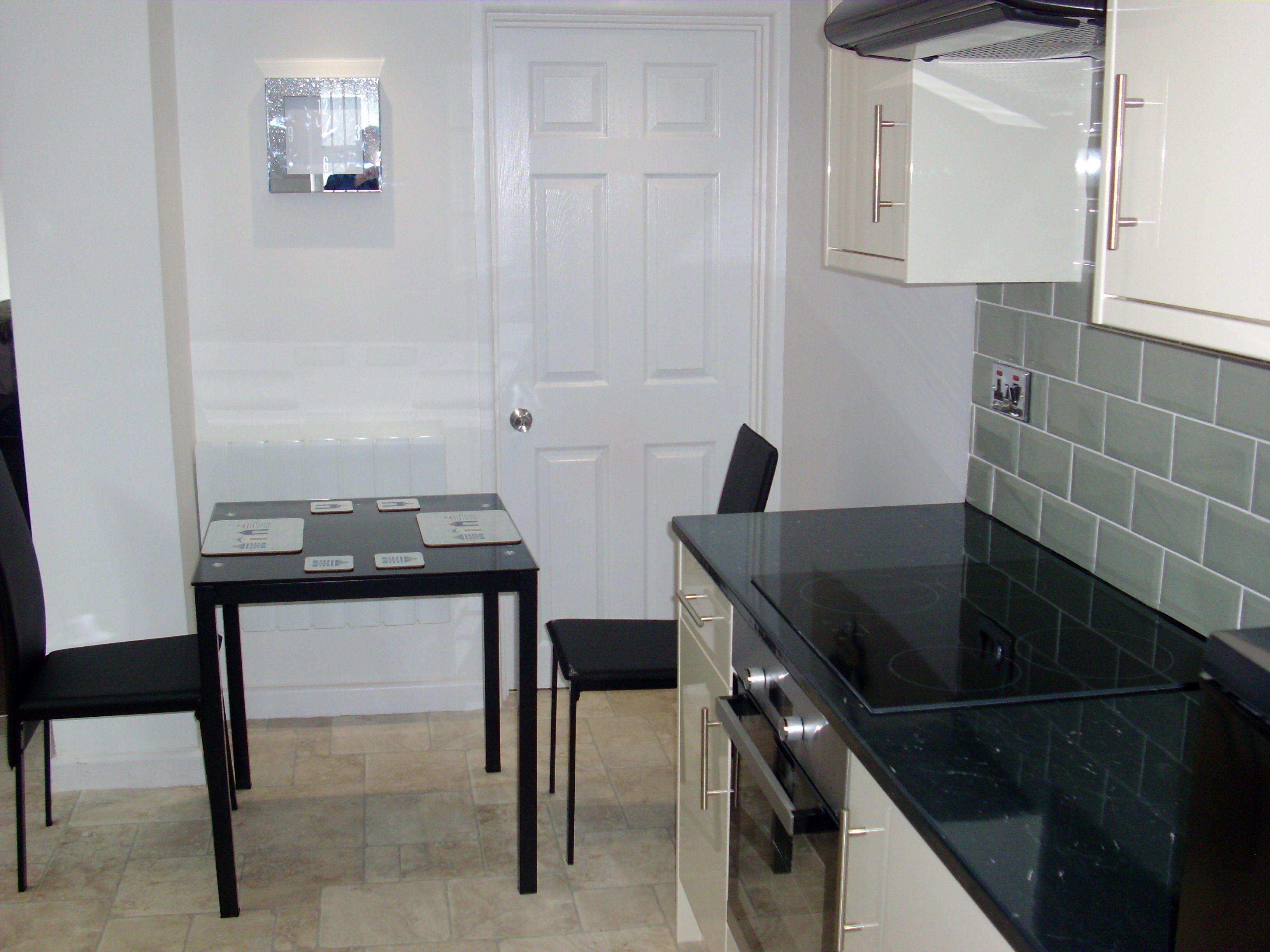 A compact kitchen with a black countertop, white cabinets, and a tiled backsplash.