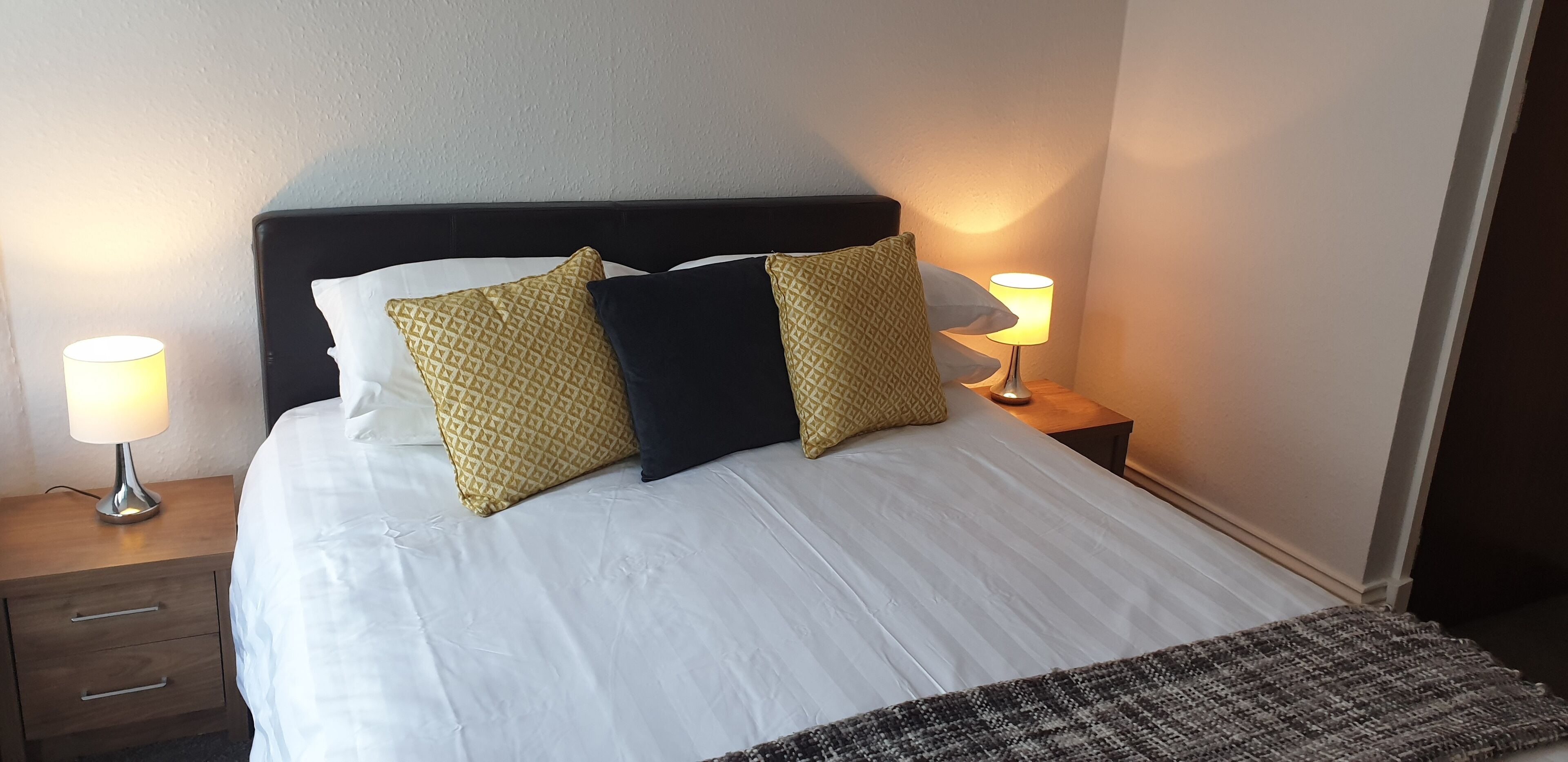 A neatly made bed with white linens and patterned pillows, two bedside lamps, and a small wooden nightstand with drawers.