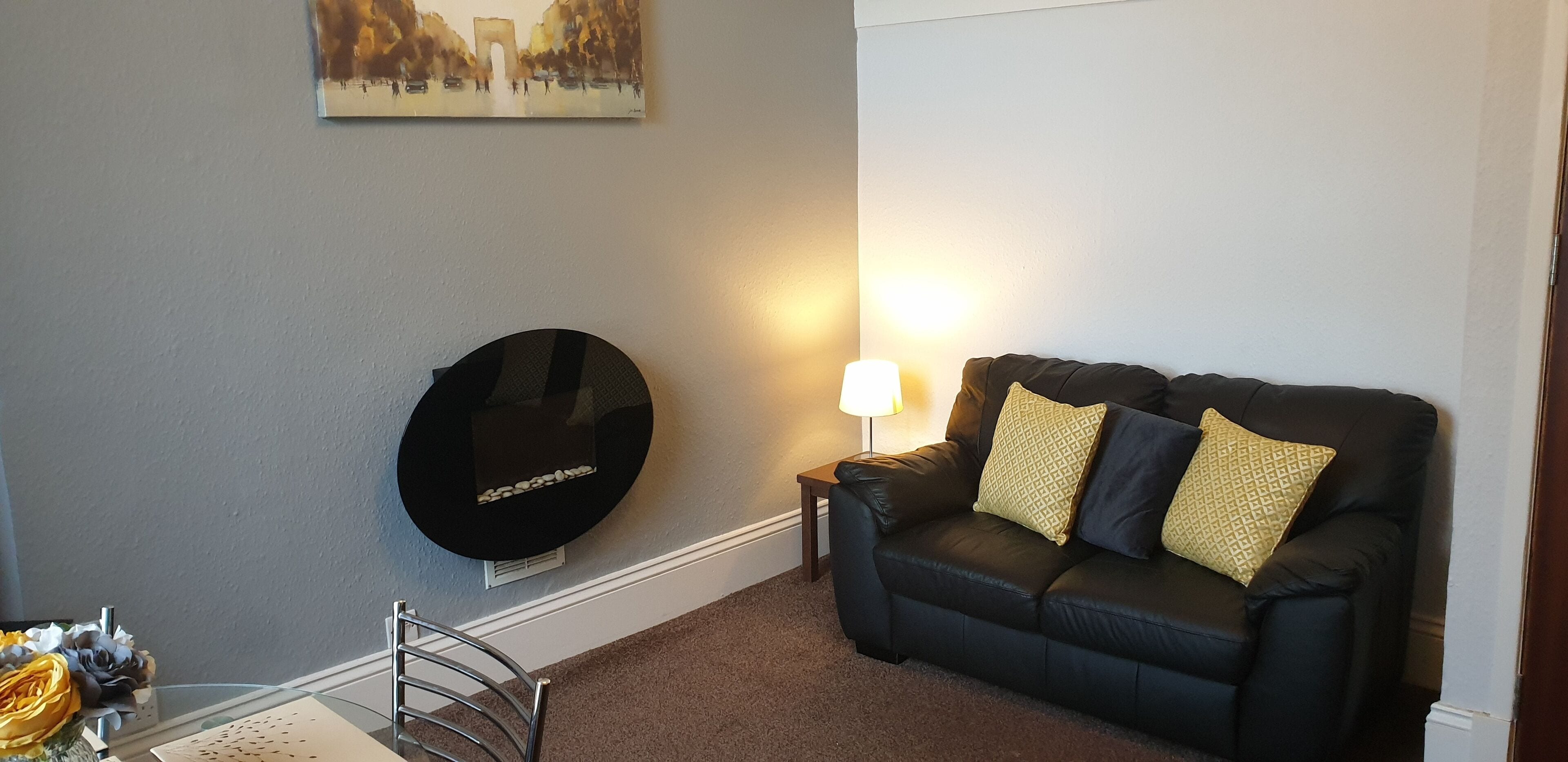 A living room with a black leather sofa, a round black TV, a lamp, and a painting on the wall.