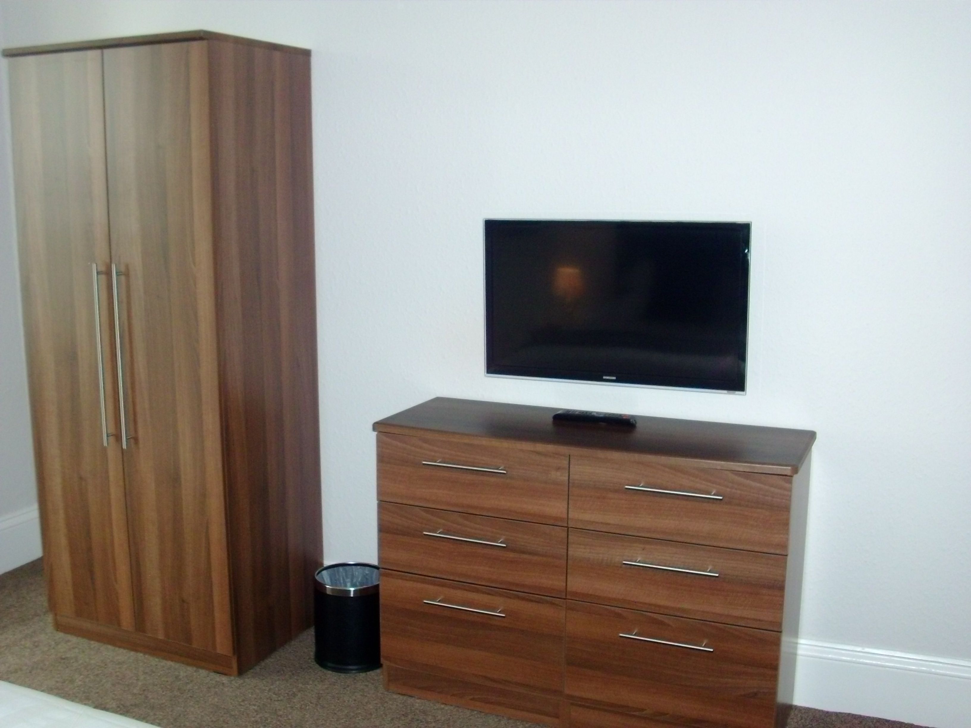 Un dormitorio con un armario, un televisor sobre un mueble bajo y un cubo de basura.