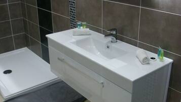 A modern bathroom with a white sink, a mirror, and a shower area.
