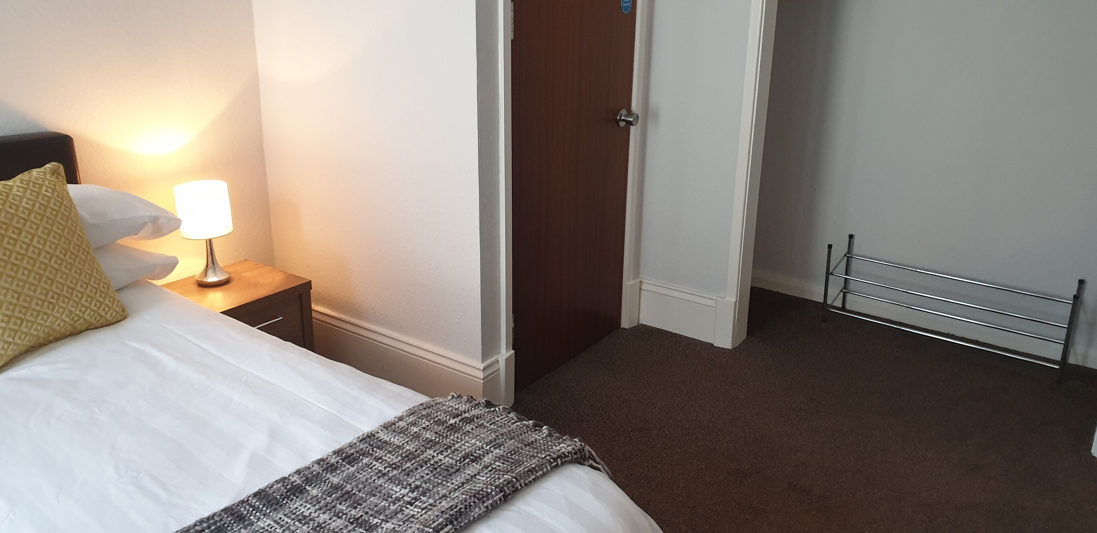 Una habitación de hotel con cama, mesita de noche con lámpara, puerta y radiador.