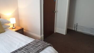 Una habitación de hotel con cama, mesita de noche con lámpara, puerta y radiador.