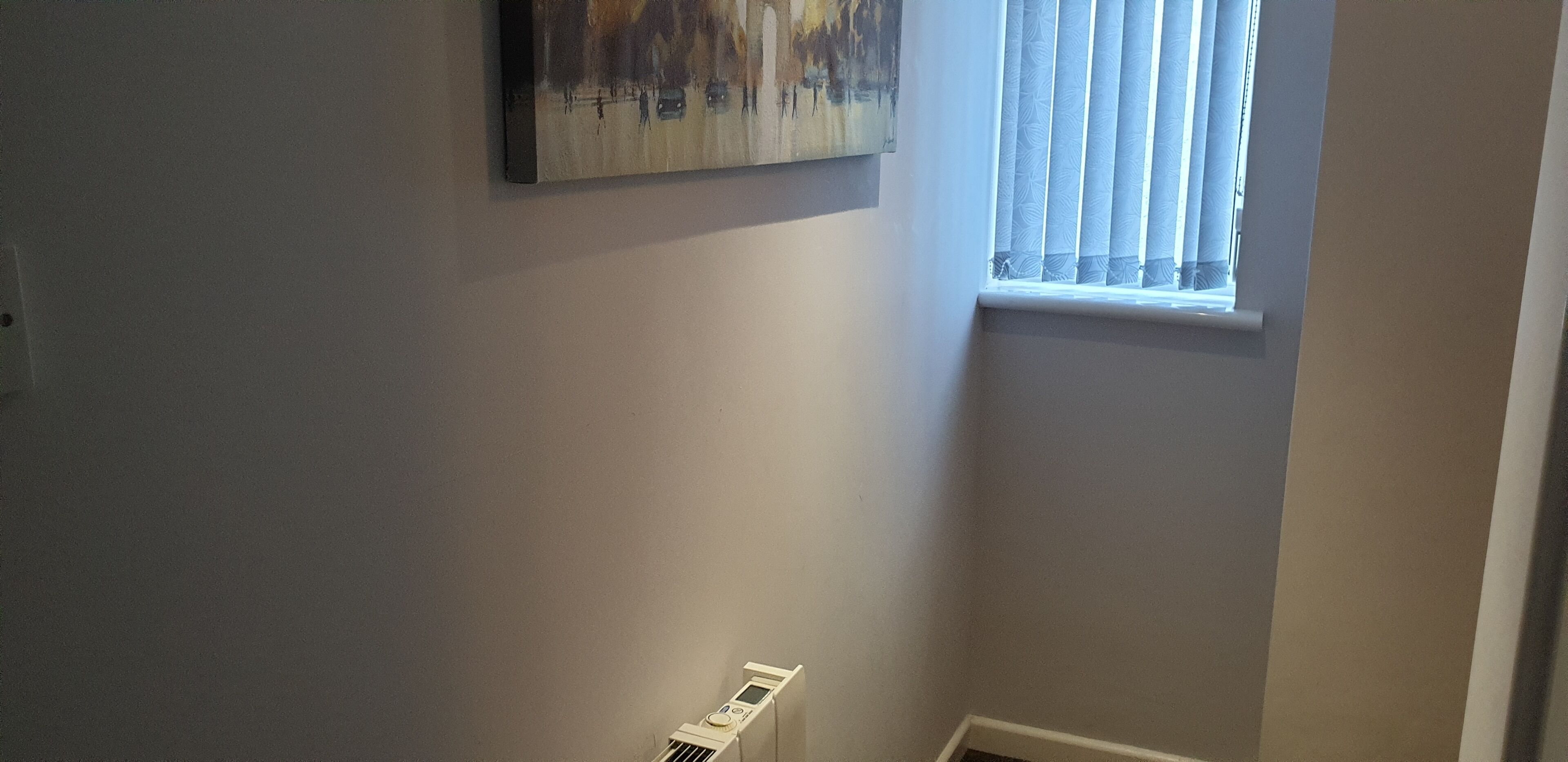 Ein Flur mit Heizkörper, einem Fenster mit Jalousien und einem Bild an der Wand.