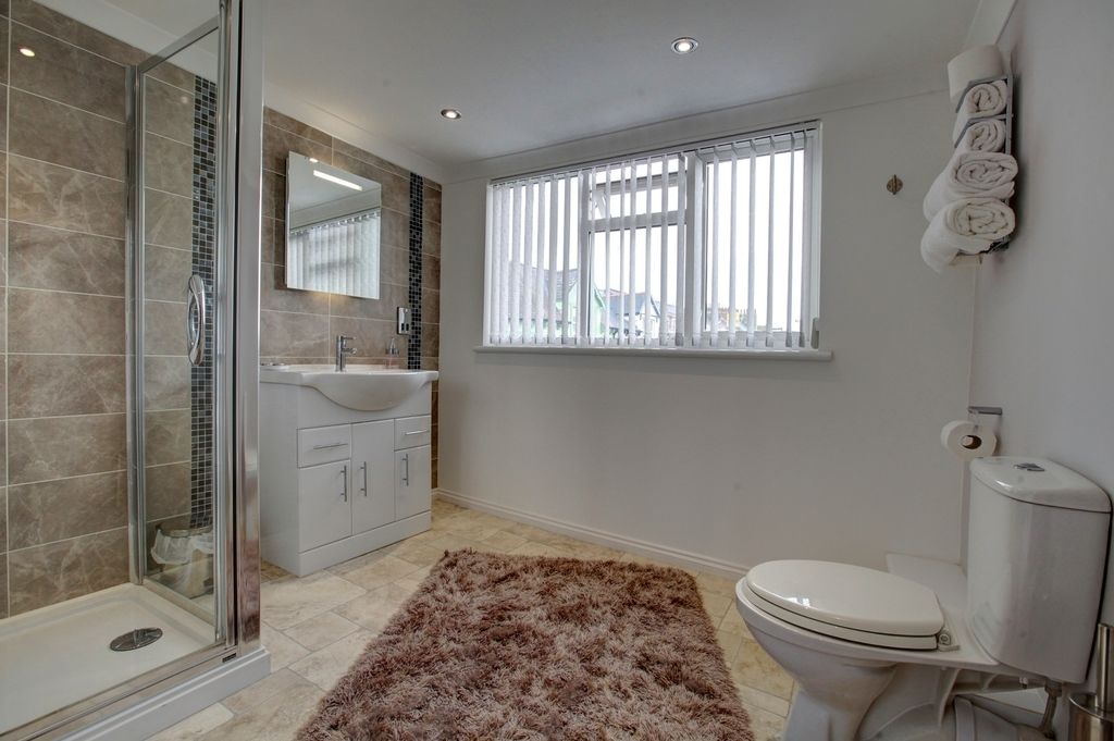 A modern bathroom with a glass shower enclosure, a white sink, a toilet, and a window with blinds.