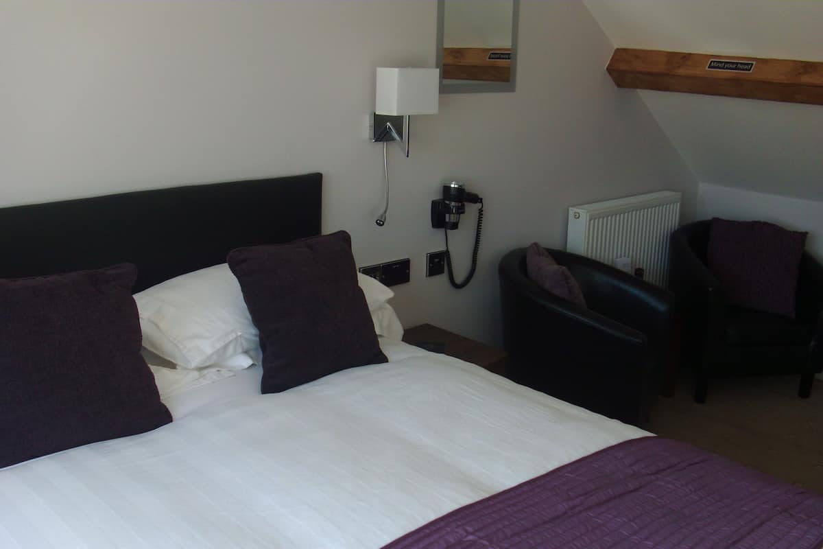A hotel room with a large bed, a chair, a desk, and a telephone.