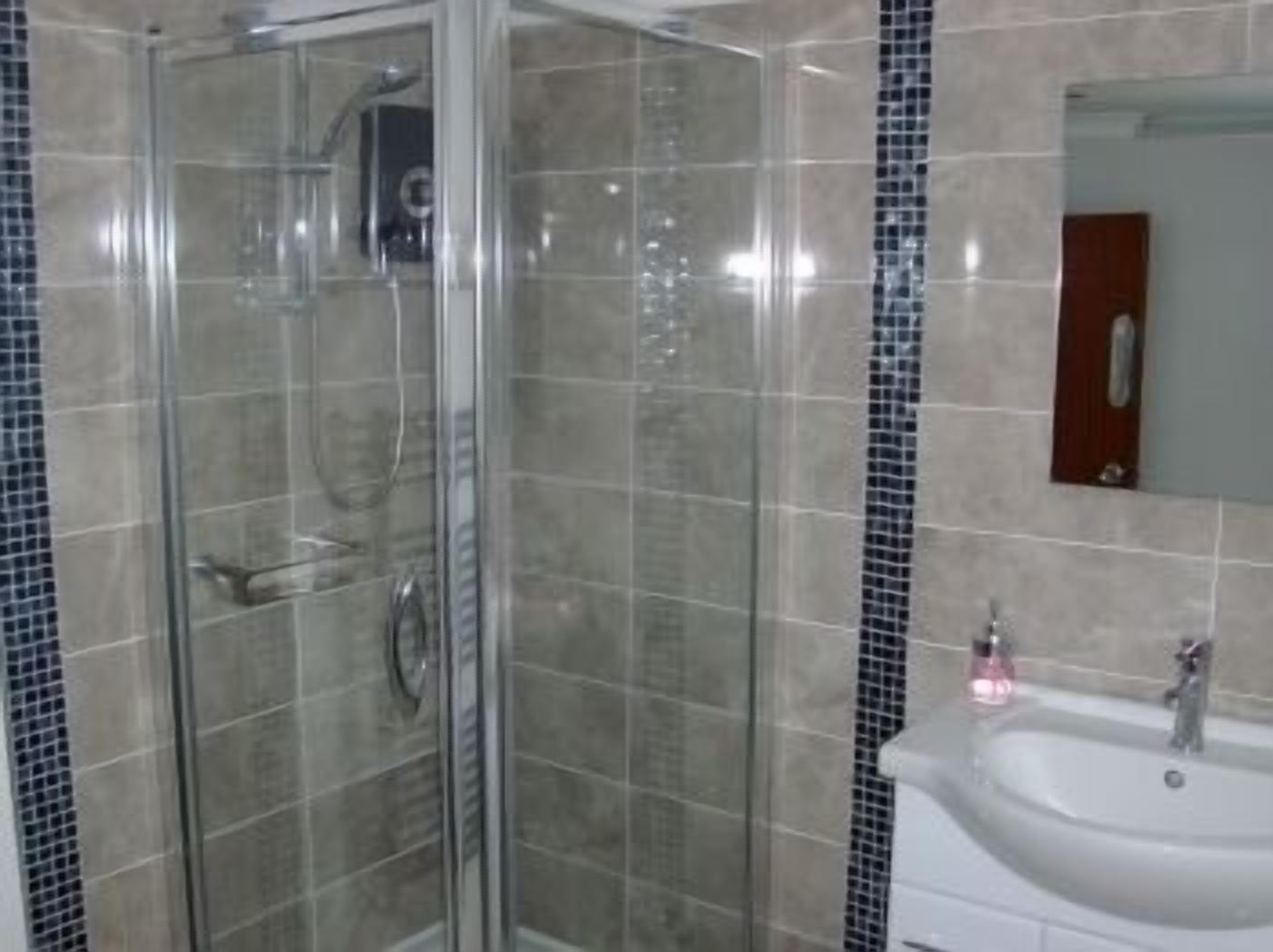 A bathroom with a glass shower enclosure, a sink with a mirror, and tiled walls.