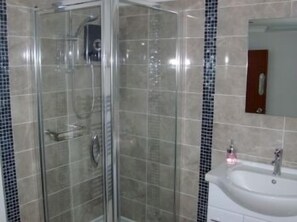 Un baño con cabina de ducha de vidrio, lavamanos con espejo y paredes cubiertas de azulejos.
