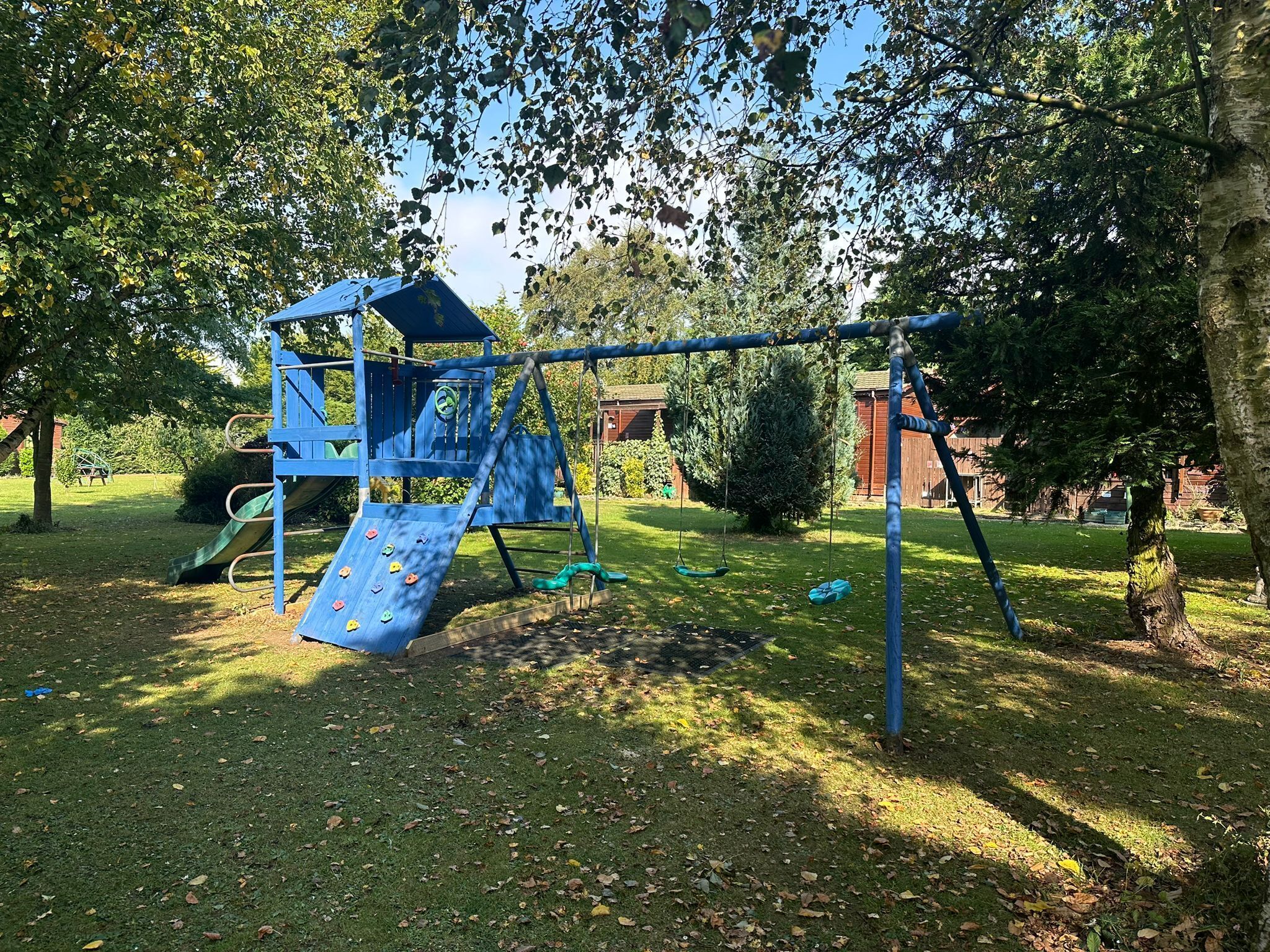 A playground with a slide and swings, surrounded by trees and a grassy area.