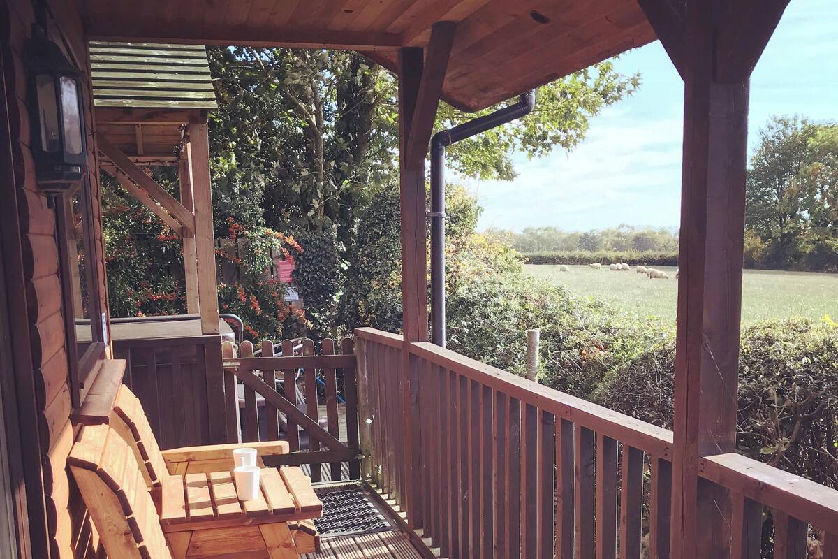 A wooden deck with a railing, wooden chairs, and a table.