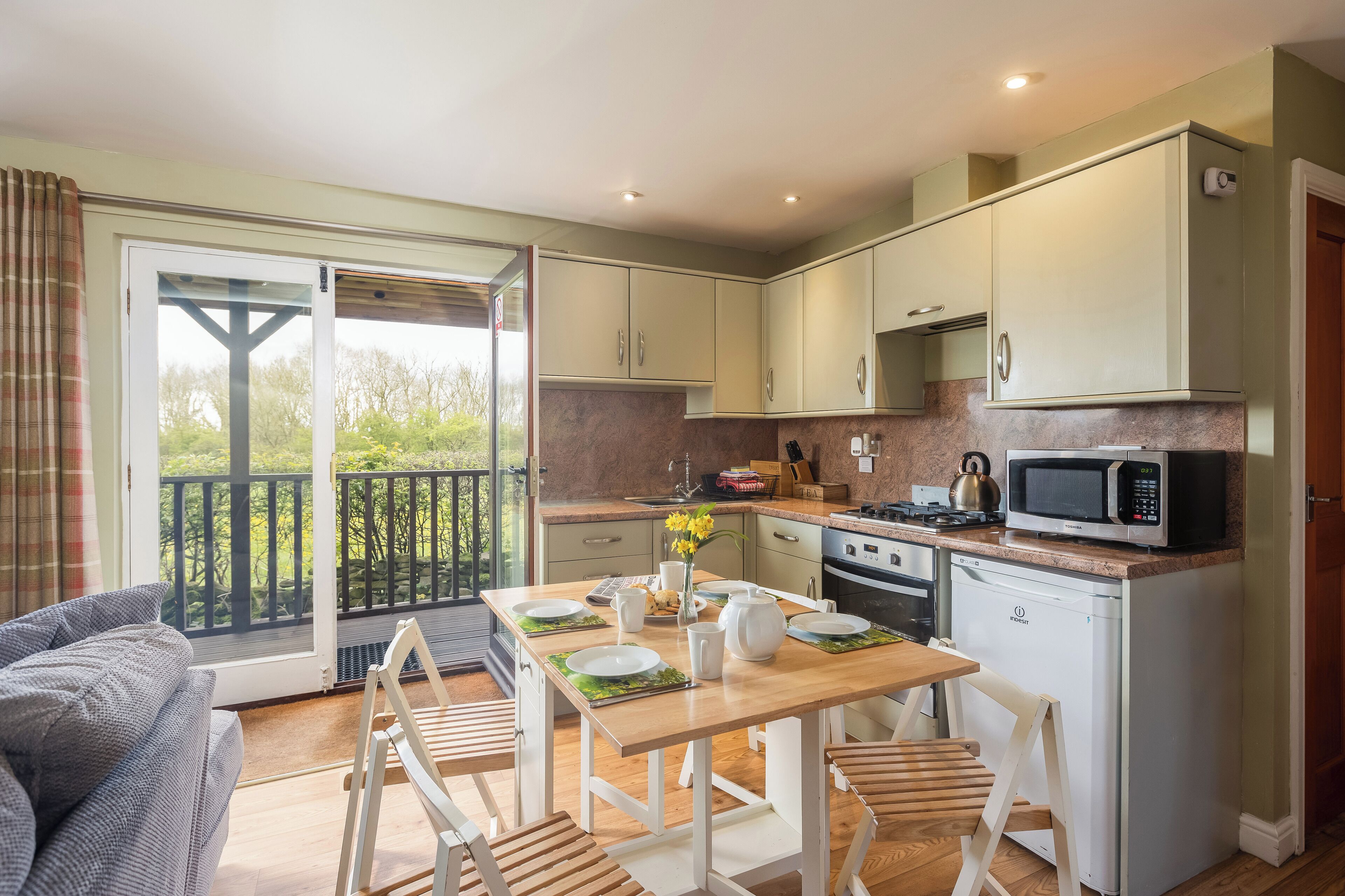 Une cuisine moderne avec un coin repas, un canapé et une vue sur la verdure grâce à la porte-fenêtre coulissante.