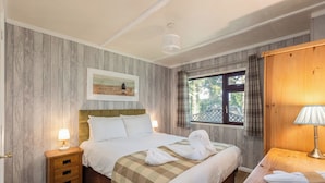 Una habitación de hotel con cabecera de madera, una cama grande con ropa blanca, una mesita de noche con lámpara y una ventana con cortinas.