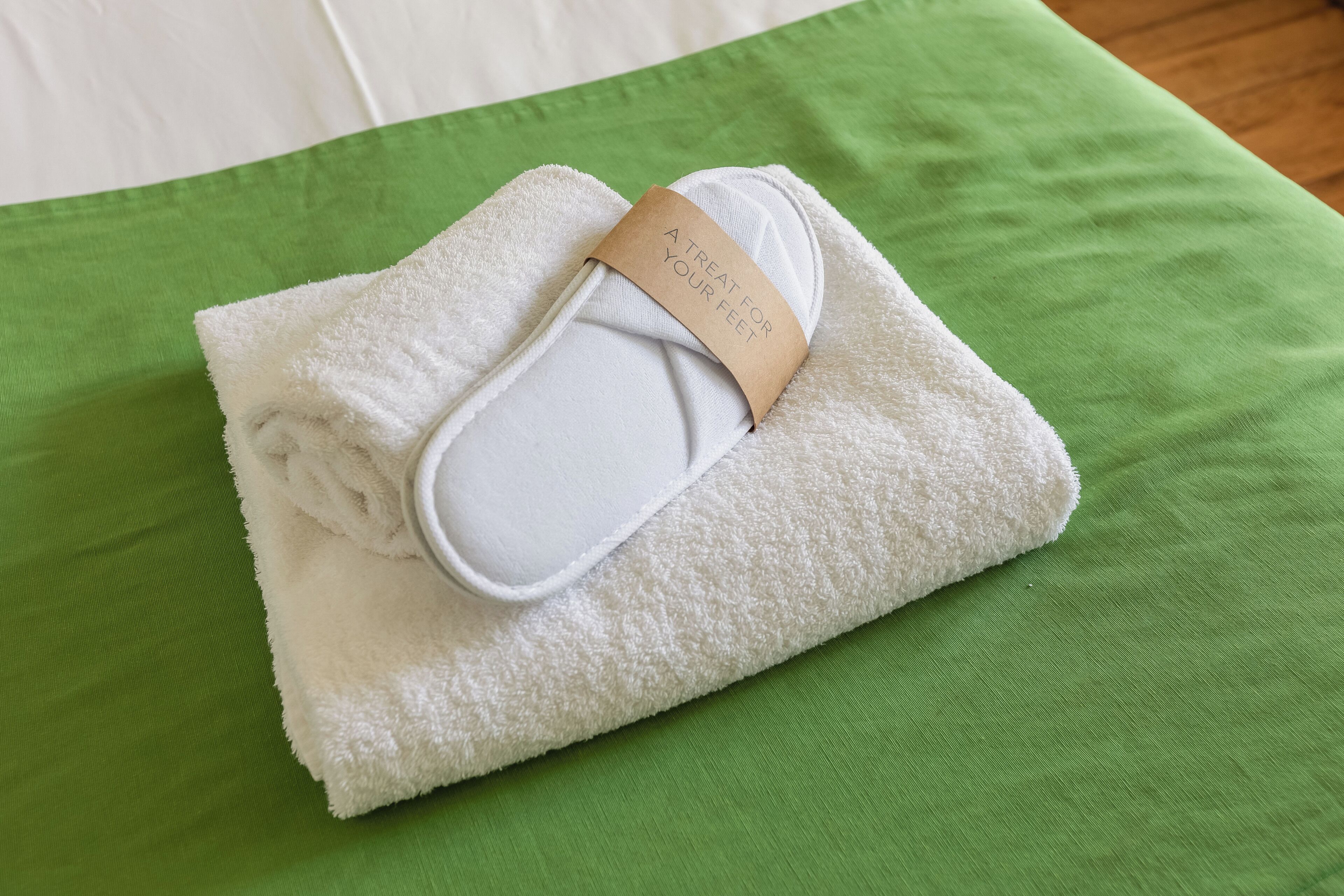 Een netjes gevouwen witte handdoek met een kaartje op een groene spreidek.