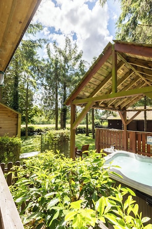 A wooden deck with a hot tub, surrounded by lush greenery and trees. - Rocklands Lodges (Pickering)