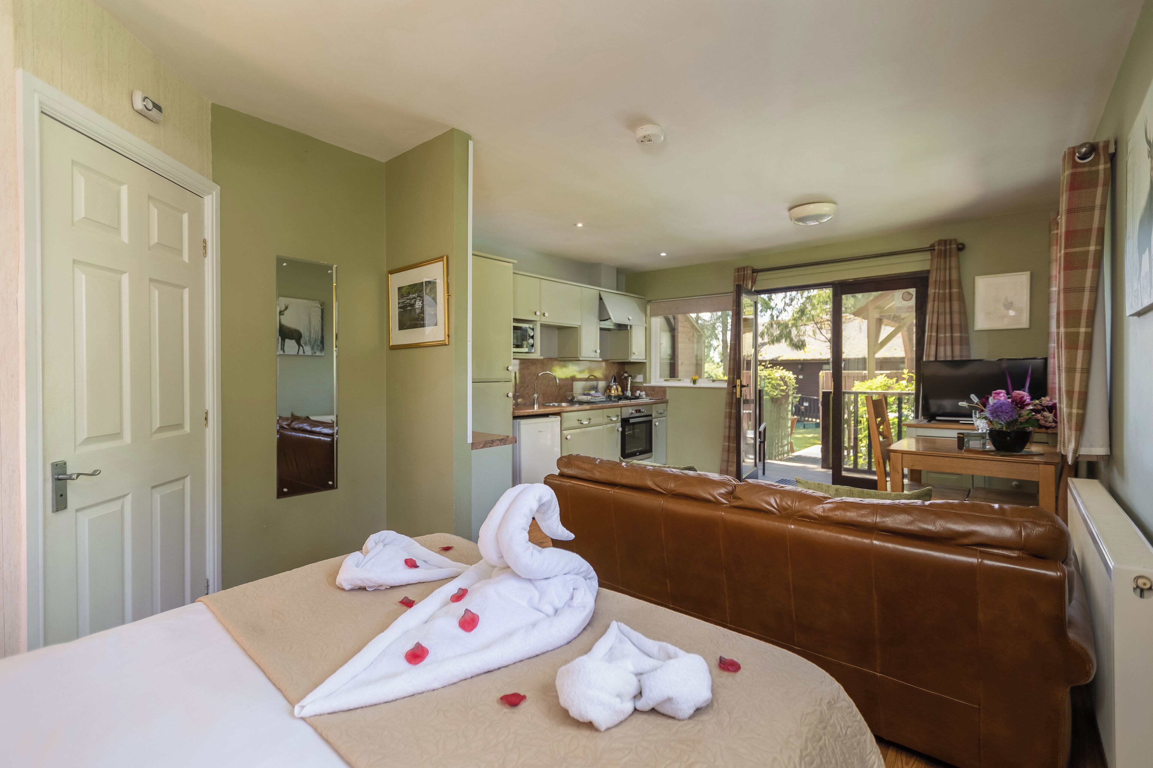 Una camera d'albergo con un letto, un divano in pelle marrone, un angolo cottura e un balcone con televisore.