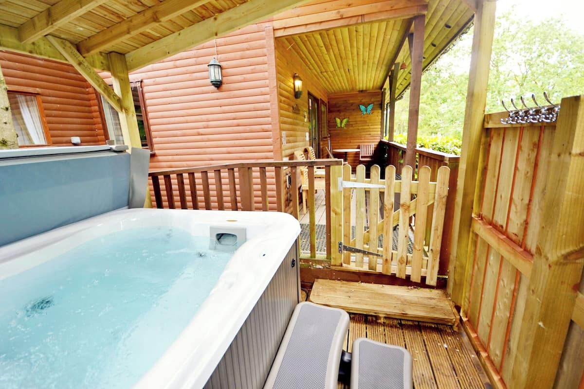 A wooden cabin with a hot tub, wooden deck, and a fenced patio area.