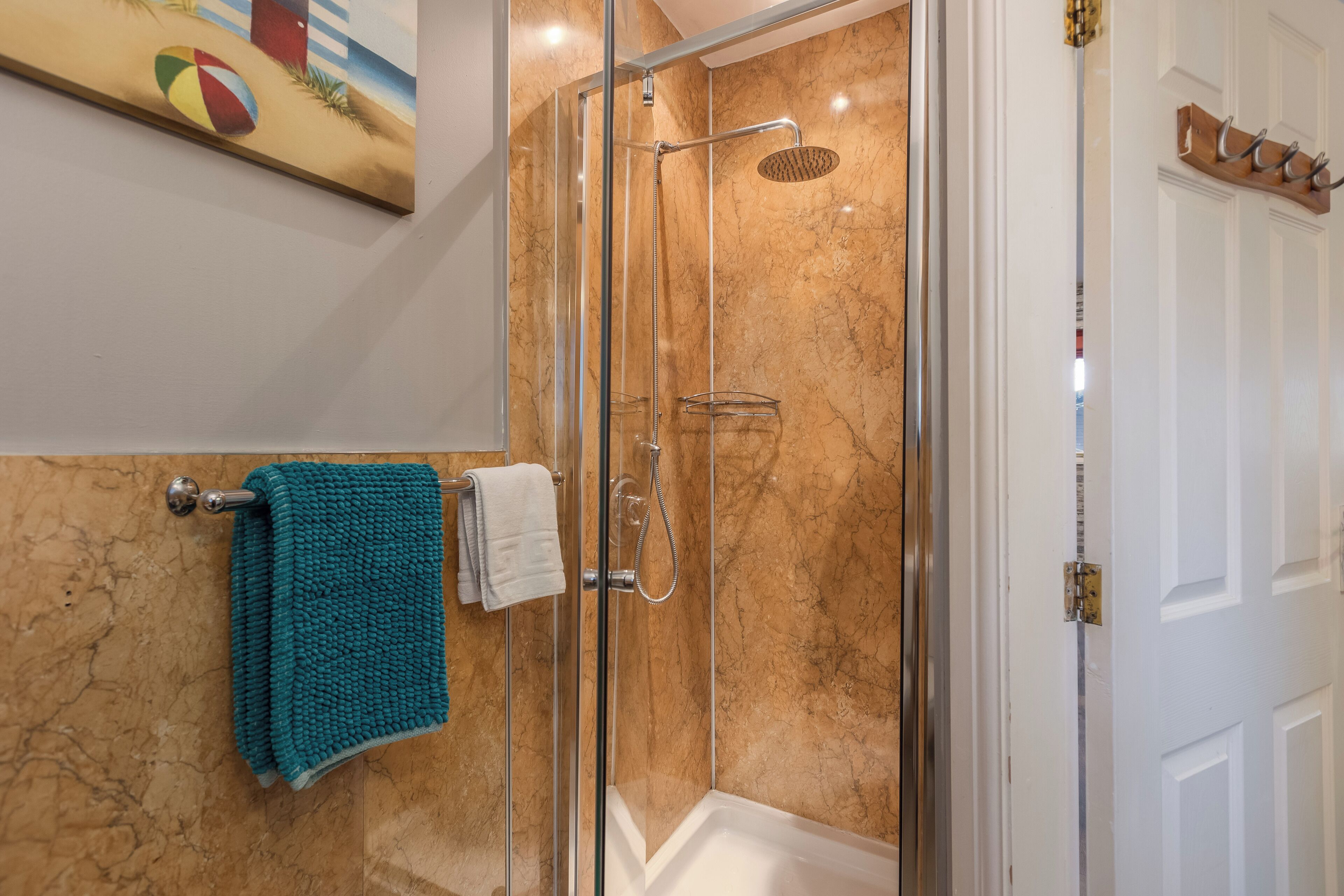 A glass-enclosed shower with a handheld showerhead, a white bathtub, and a towel rack with a teal towel.